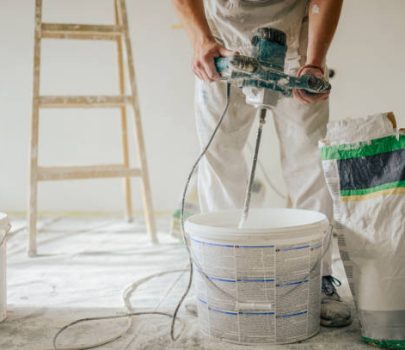 Builder's hands using manual cement mixer for mixing plastering materials and preparing it for skim coating and plastering walls in a house in renovation process. Cropped picture of man mixing plaster